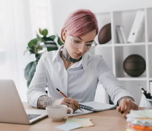 Tattoo artist with pink hair sketching at desk
