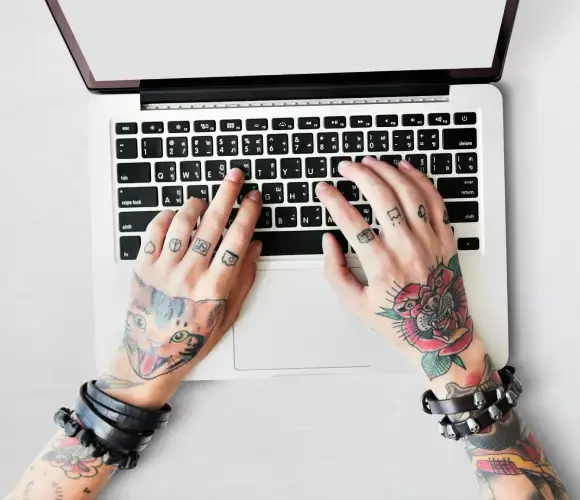 Tattooed hands typing on laptop keyboard